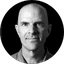 Black and white headshot of a bald man against a dark background.