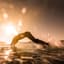 Man diving into water creating large splash against bright sunset over the sea