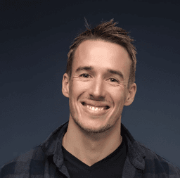 Portrait of smiling man with short brown hair wearing a plaid shirt against a dark background.