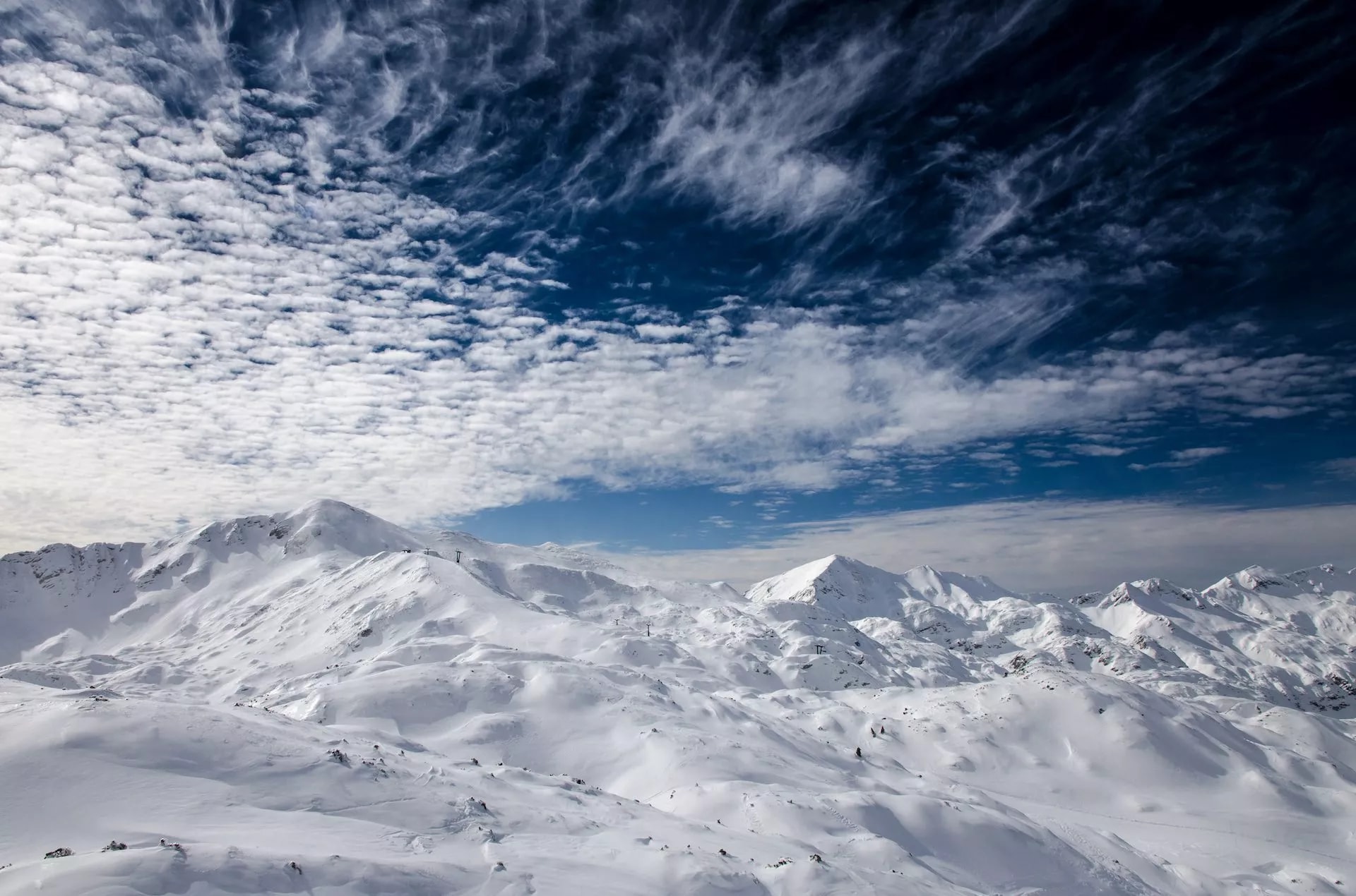 Snowy mountain peaks under dramatic blue sky with scattered white clouds at Vogel ski resort in winter.