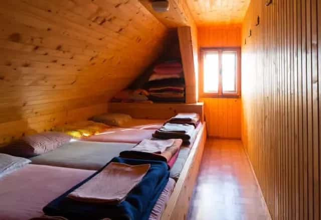 Attic dormitory room with wooden walls, built-in beds, and bright window light, Prešernova Koča na Stolu.