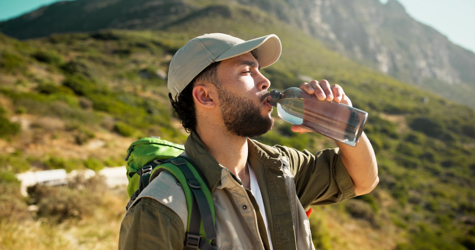 Berg, Trinkwasser und Mann mit Pause beim Wandern, Hydration oder Sommertourismus für Reisen. Draußen, Wellness und Person entspannt mit Flüssigkeitsflasche, Trekking oder durstig bei Sightseeing-Urlaub