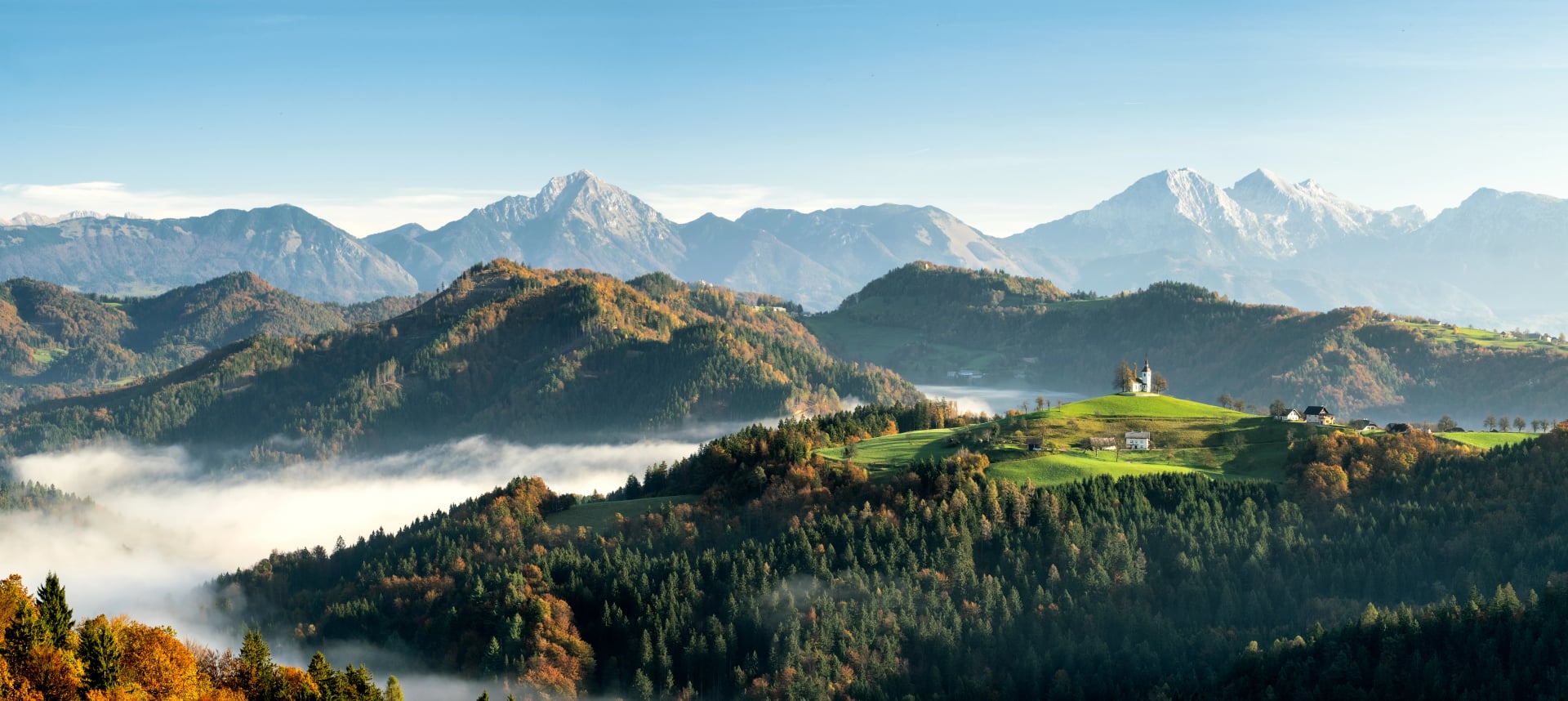 Die Kirche Sveti Tomaz mit tief liegendem Nebel und den Alpen im Hintergrund während des Sonnenaufgangs in der Herbstsaison Slowenien