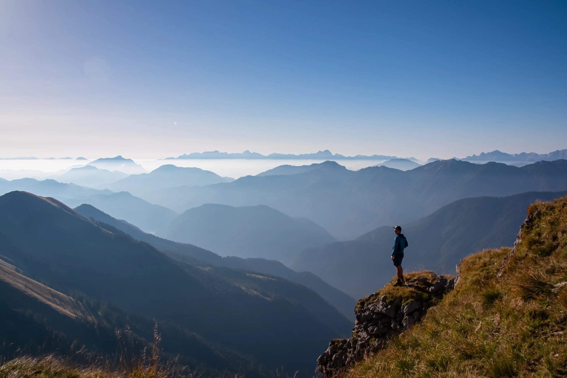 Silhouette eines Wanderers im alpinen Landschaft der Gailtaler Alpen, Kärnten, Österreich. Panoramablick auf majestätische, neblige Gebirgszüge der Julischen Alpen, Karawanken, Karnischen Alpen. Friedliche, ruhige Atmosphäre