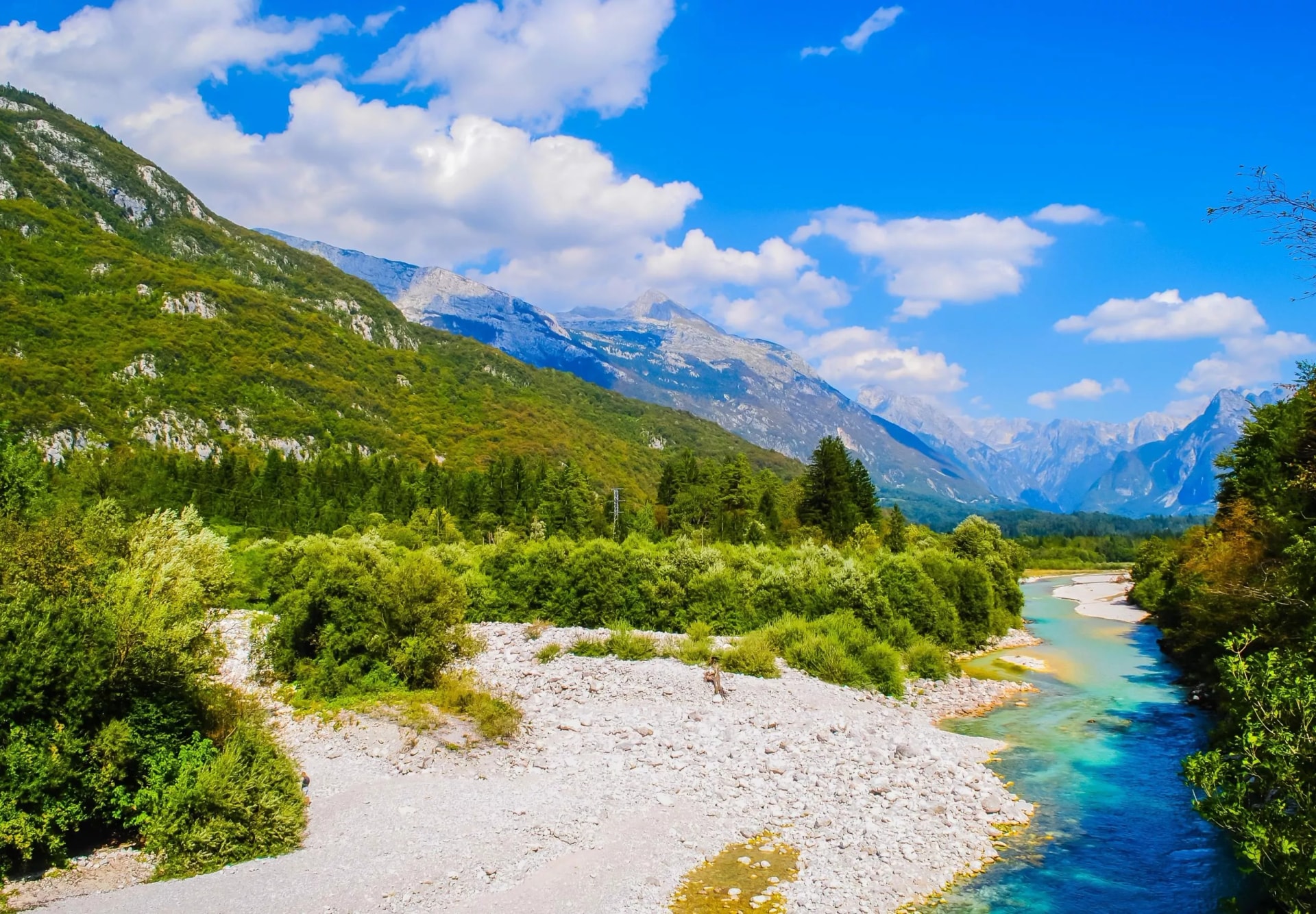 Turquoise river flowing through a valley with lush green mountains under a blue summer sky.